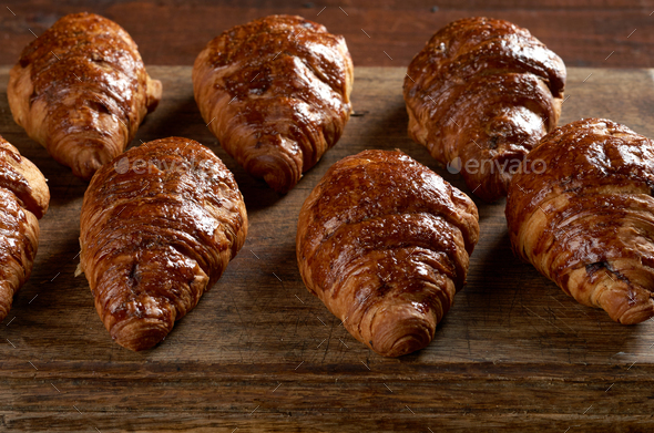 Baked croissants on a wooden brown board, delicious and appetizing pastries