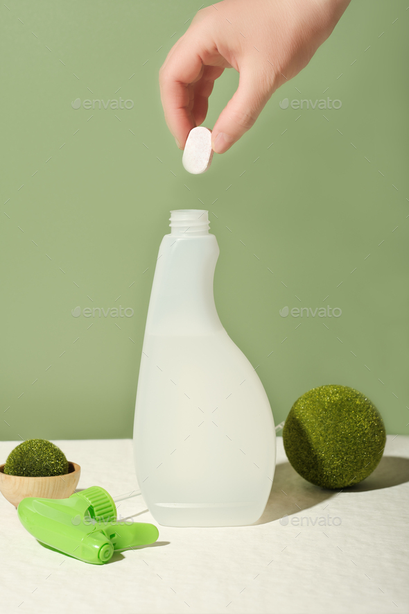 hand holding dissoluble tablet for kitchen cleanser refill. bottle of cleansing spray refilling.