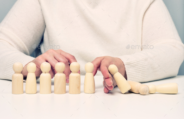 Hand stops the fall of wooden figurines of men on a white background