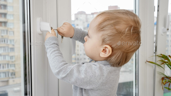 Little baby boy opens window safety lock with key. Baby in danger. Child safety and protection - Stock Photo - Images