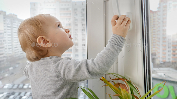 Little baby pressing knob and pulling window handle trying to open window. Child in danger at home. - Stock Photo - Images