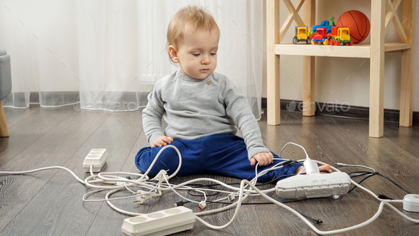 Little baby boy left alone playing with electric cables and wires. Child in danger - Stock Photo - Images
