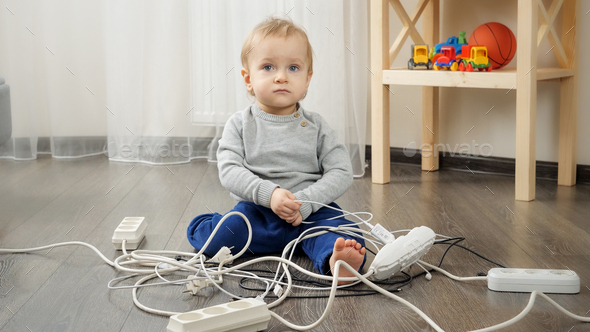Little baby boy playing with electric plugs and wires at home - Stock Photo - Images