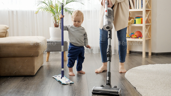 Little baby boy helping his mother doing cleanup at home and vacuming carpet. - Stock Photo - Images