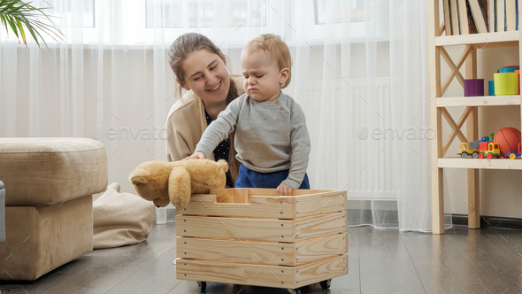 Little baby boy with mother collecting toys in wooden toy box at living room - Stock Photo - Images