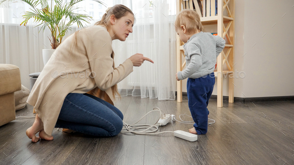 Young caring mother telling her baby son not to play with electricity, wires and cables - Stock Photo - Images