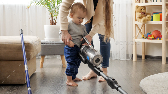 Young mother doing housework teaching and giving vacuum cleaner to her baby son. - Stock Photo - Images