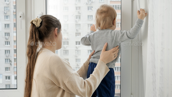 Little baby boy with mother looking out of the window of high store building. - Stock Photo - Images