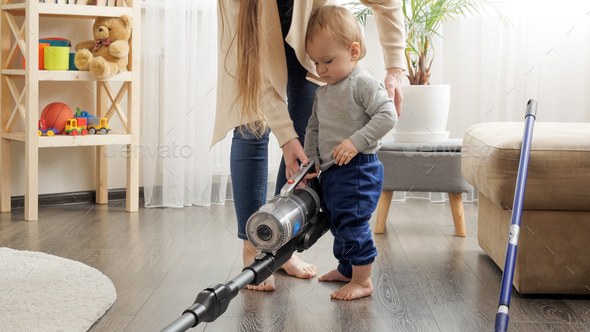 Cute baby boy holding vacuum cleaner and helping his mother doing cleanup - Stock Photo - Images