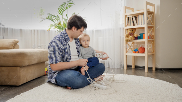 Young caring father teaching his baby son not to touch electric plugs, wires and cables at home. - Stock Photo - Images