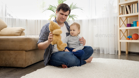 Happy smiling baby boy with father having fun and playing with teddy bear on carpet at home. - Stock Photo - Images