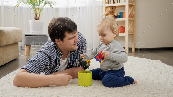Young father lying on carpet with his baby son and playing with toys - Stock Photo - Images