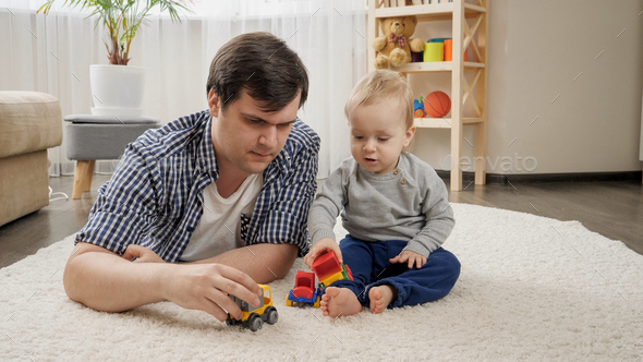 Young father lying with his baby son on carpet and playing toy cars. - Stock Photo - Images