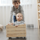 Older boy riding his baby brother in wooden toy cart in living room. - PhotoDune Item for Sale