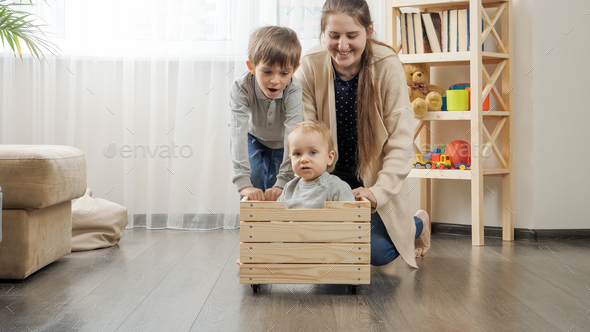 Cute baby boy sitting in wooden toy box while his family riding him at living room. - Stock Photo - Images