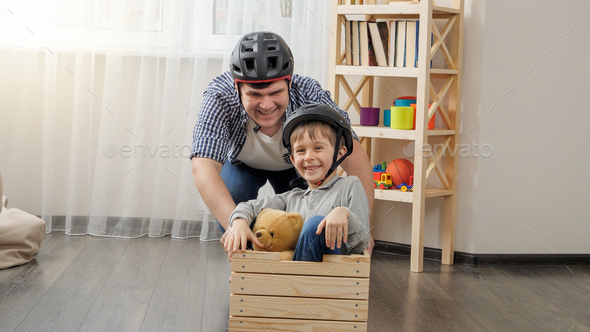 Funny shot of young father playing with his son and having race in wooden cart at home. - Stock Photo - Images
