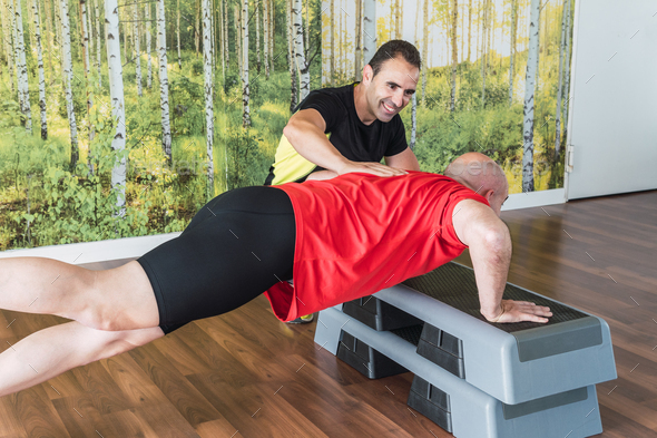 Personal trainer helping a man do push-ups indoors