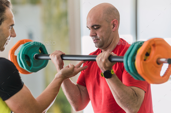 Man lifting weights with the help of a coach
