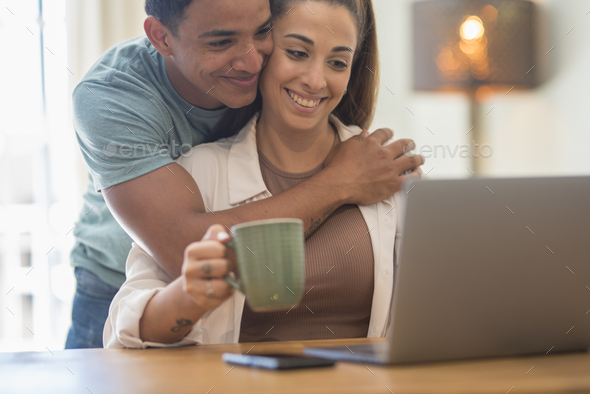 Young interracial couple live together at home and smile looking a laptop on the table.