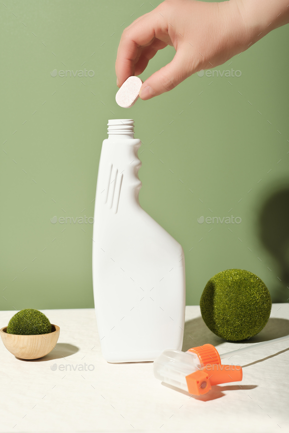 hand holding dissoluble tablet for cleaning detergent refill. bottle of cleansing spray refilling