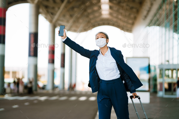 Grey asian woman in face mask waving for taxi on airport parking
