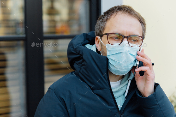 Sad puzzled man in panic because of epidemic disease, covers face with medical mask.
