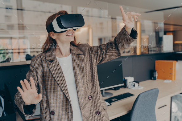 Happy female office worker in VR headset enjoying virtual reality game ...
