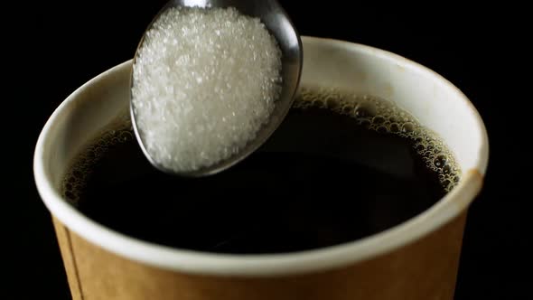 Sugar is put in a glass of black coffee.