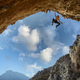 Male rock climber hanging with one hand on on a cliff against sky - PhotoDune Item for Sale