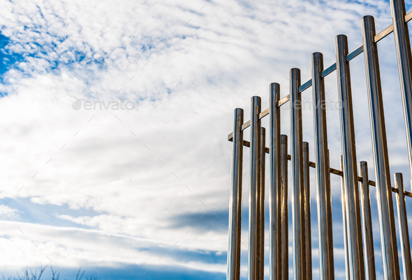 Fence with tall metal bars pointing to the blue sky with perspective viewed from below.