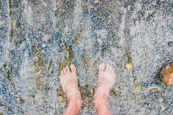 Bare feet cooling off in a stream full of pebbles, revitalizing massage in nature.