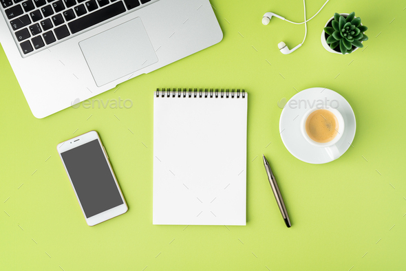 Concept of modern workspace. Notebook, smartphone, coffee cup, laptop earphones on green backdrop
