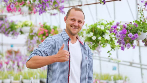 Young Agronomist Businessman Stands Smiling in Flower Greenhouse Looking at Camera Show Thump Up alt