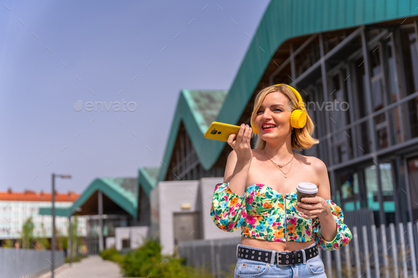 Pretty blonde woman walking and sending a voice note with the phone in the city