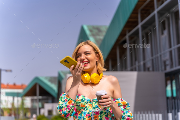 Pretty blonde woman walking and sending a voice note with the phone in the city