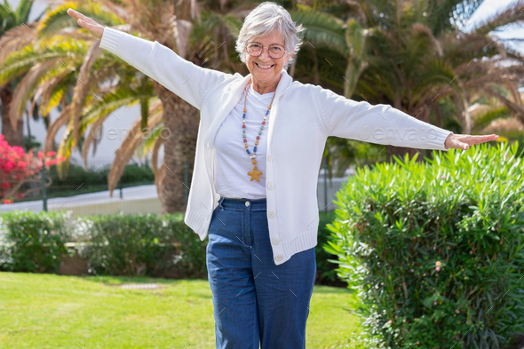 Happy senior woman walks on the curb with her arms outstretched to keep balance.