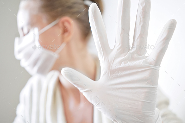 corona virus covid-19 pandemic. woman in white medical mask and gloves showing gesture stop.