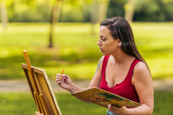 Woman in summer clothes painting in a park