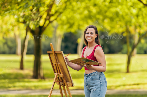 Woman in summer clothes painting on a canvas outdoors