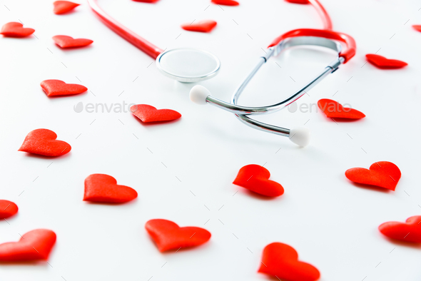 Red stethoscope surrounded by hearts seen from above isolated on white background