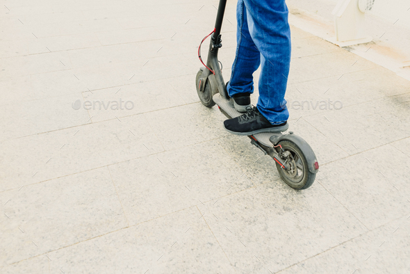 Man in jeans on an electric scooter through the city, copy space, electric urban mobility.