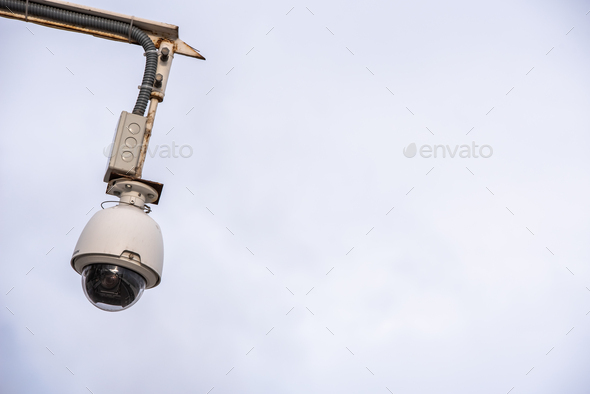 Security camera hung to monitor people in a city, isolated over blue sky
