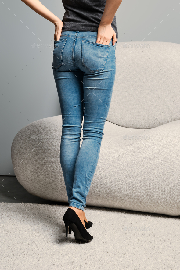 Cropped image of female legs in denim jeans standing half turning back