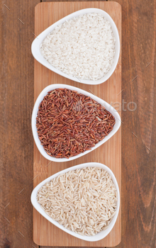 Three bowls with different types of rice: crude, red and round rice on wooden board