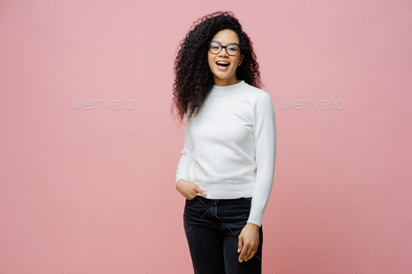 Woman going to work, laughs at something positive, wears neat white jumper and jeans.