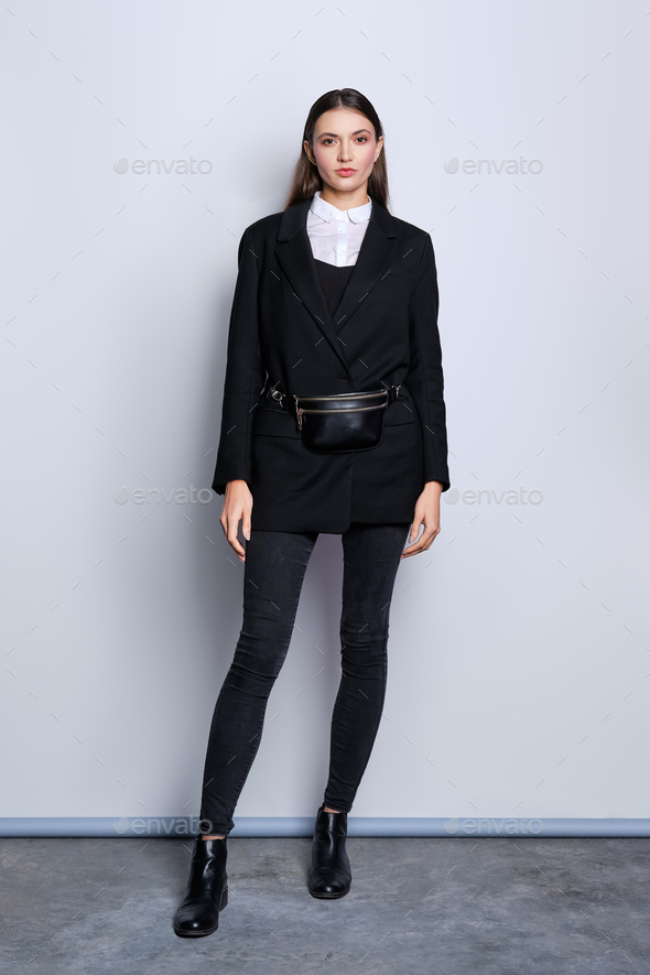 Portrait of trendy girl in black jacket, jeans, white shirt and waist bag