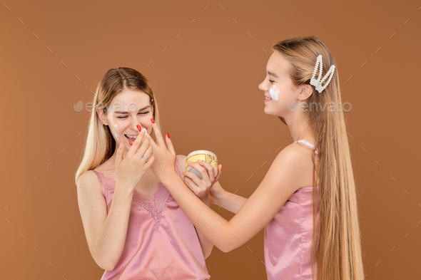 Two young girls foolishly applying face of each other with acne cream