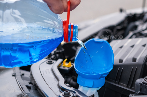 Close up driver pouring blue non freezing windshield glass washer fluid into the tank of the car