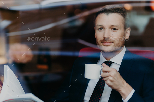 Attractive businessman in formal suit, drinks coffee during dinner break, sits in luxury cafe.