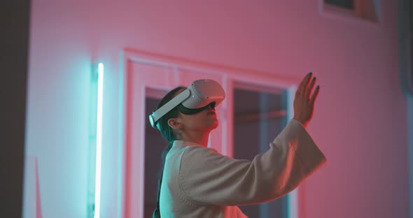 Young woman stting on a desk wearing vr goggles in blue and pink neon light alt